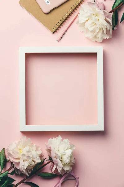 Kreatywne płaskie leżały z kwiatami, notatnikiem, okularami, telefonem komórkowym i białą drewnianą ramą na różowym tle — Zdjęcie stockowe