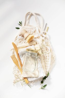 Sıfır atık, çevre dostu konsept. Cam kavanozlar, ağ torbaları, doğal fırça ve beyaz arka planda bambu çatal bıçak takımı.