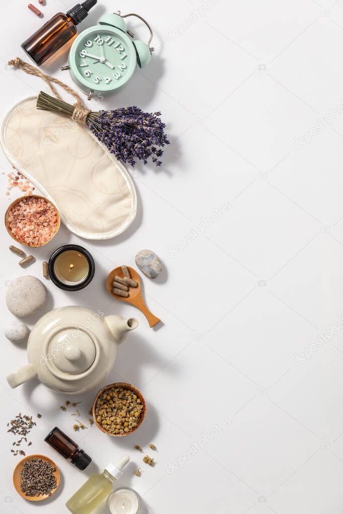 Herbal medicine for treat depression and insomnia concept. Alarm clock, medicine herbs, capsules, camomile tea and aromatherapy oil on white background, flat lay