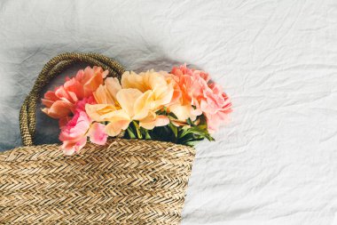 Gri keten masa örtüsü arkaplanının üzerinde saman çantada duran güzel şakayık çiçekleri.