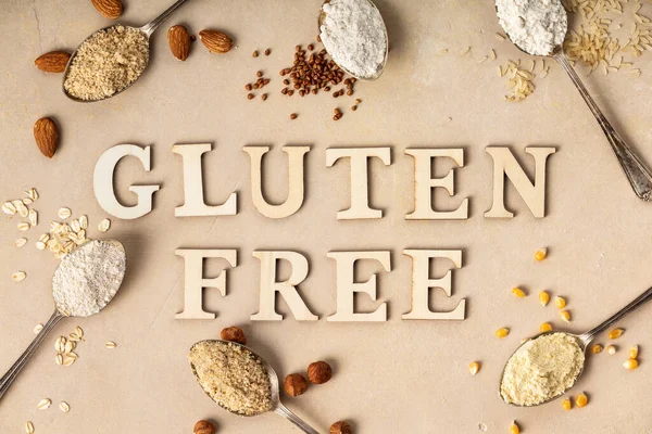 Metal spoons of various gluten free flour (almond flour, oatmeal flour, buckwheat flour, rice flour, corn flour) and gluten free lettering made of wooden letters