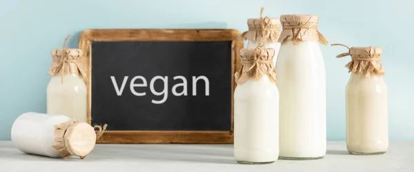 Non dairy plant based milk in bottles and chalkboard with Vegan lettering on light blue background