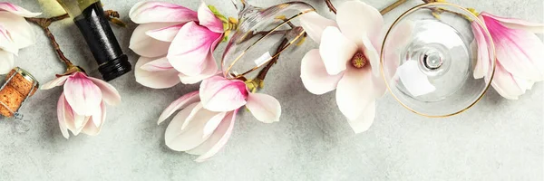 Beautiful flat lay with spring magnolia flowers, wine and glasses on grey stone background — Stock Photo, Image