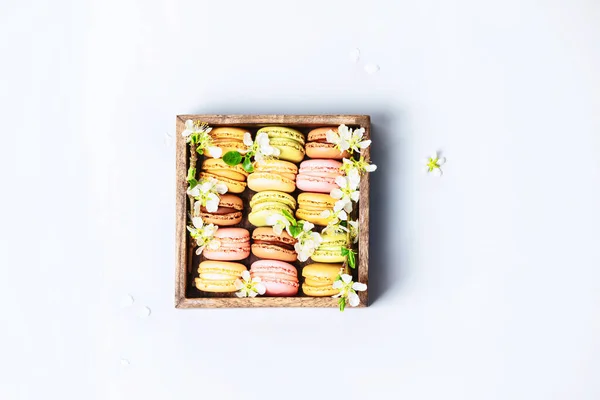 Macaroons em caixa de madeira com flores de primavera flat lay — Fotografia de Stock