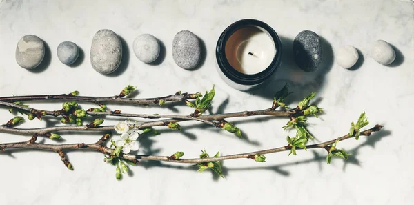 Flat lay composition with beautiful spring cherry branches, natural candle and grey stones on white marble background. — Stock Photo, Image