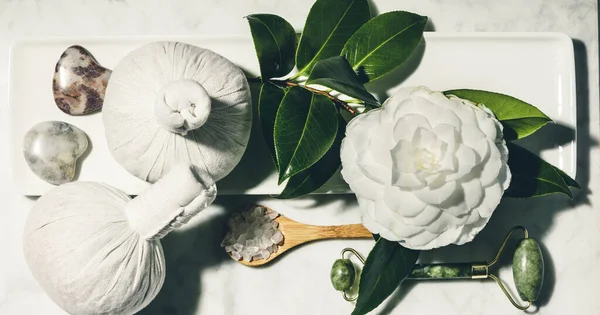 Επίπεδη σύνθεση με ανοιξιάτικο λουλούδι καμέλια και διάφορα προϊόντα περιποίησης ομορφιάς σε λευκό μαρμάρινο τραπέζι — Φωτογραφία Αρχείου