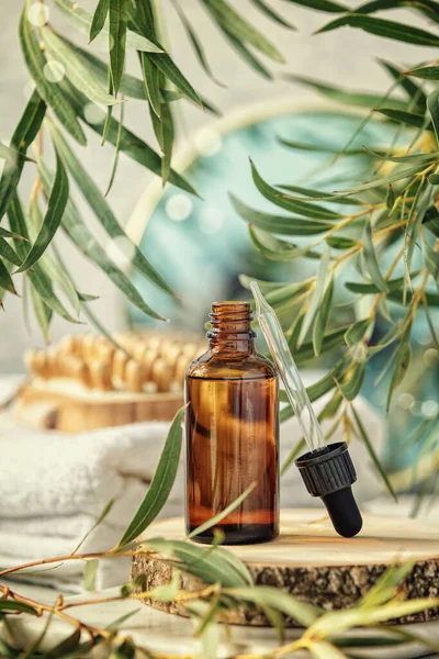 Amber glass bottle with wooden massage brush, eucalyptus leaves, mirror and towels. Eco friendly massage and body care concept — Stock Photo, Image
