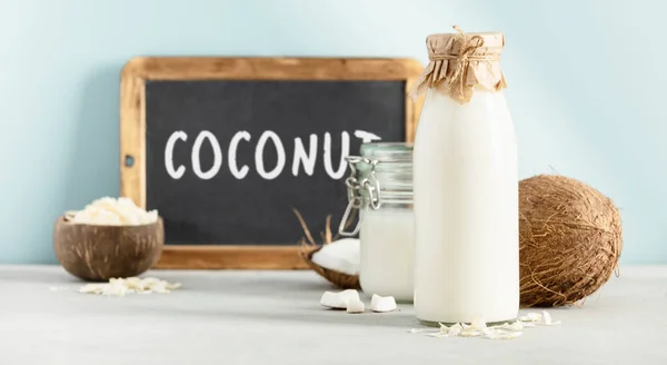 Kokosnussprodukte frische Kokosnuss, Öl, Milch und Kreidetafel mit Coconut Schriftzug auf blauem Hintergrund — Stockfoto