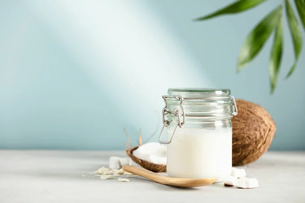 Kokosöl im Glas mit frischer Kokosnuss und tropischen Blättern, alternatives Therapiekonzept auf blauem Hintergrund — Stockfoto