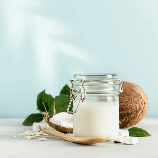 Coconut oil in jar with fresh coconut and tropical leaf shadow, square composition — Stock Photo, Image