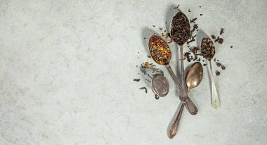 Hafif bir taş yüzeyde antika kaşıklarda sergilenen bol yapraklı çayların çeşitliliği, refah, bitkisel karışımlar veya çay temalı içerikler için idealdir..