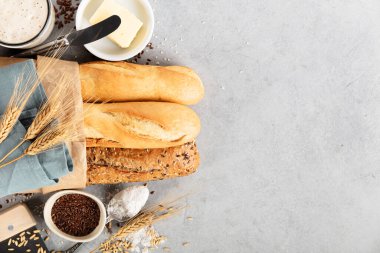 Tereyağı, un, tahıl ve tohum dolu bir kesekağıdındaki üç taze ekmek hafif bir yüzeye dizilmiş.