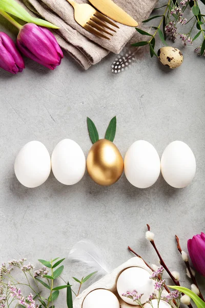 Beyaz ve altın yumurtalarla süslü Paskalya dairesi, pembe laleler, bahar yeşilliği ve hafif taşlı arka planda altın çatal bıçak seti. Kopya alanı ile modern festival konsepti.