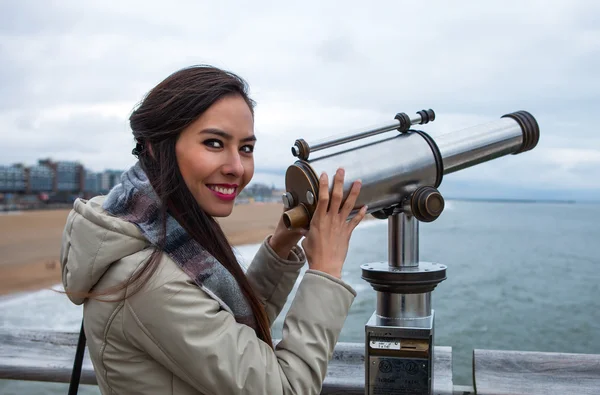 Beautiful young woman with magnificent hairs near telescope on pier in the Hague. — Stock Photo, Image