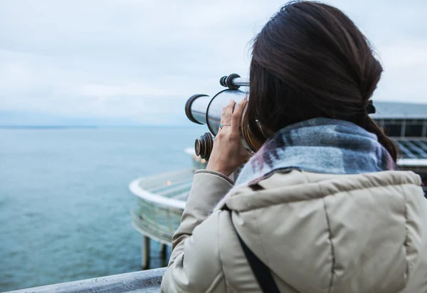 Schöne junge Frau mit prachtvollen Haaren in der Nähe von Teleskop auf Pier in Den Haag. — Stockfoto