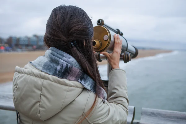 Schöne junge Frau mit prachtvollen Haaren in der Nähe von Teleskop auf Pier in Den Haag. — Stockfoto