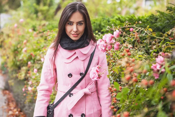 Vonzó fiatal nő gyönyörű hosszú hajat öltözött, rózsaszín kabát jelentő szabadtéri. — Stock Fotó