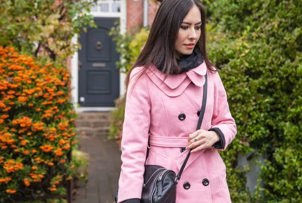 Attraktiv ung kvinna med långa vackra hår klädd rosa kappa poserar utomhus. — Stockfoto