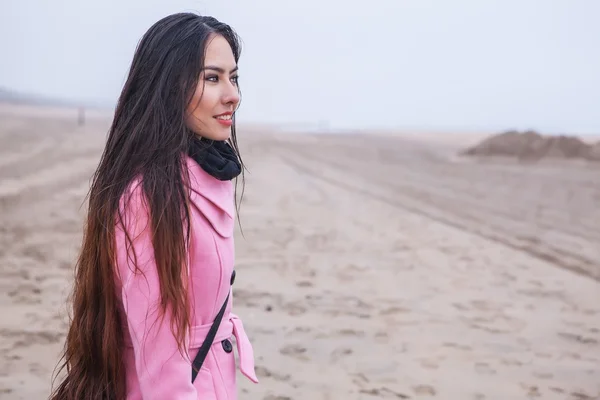 Gyönyörű hosszú hajat vonzó fiatal nő portréja öltözött rózsaszín bevon, melyik pózol őszi északi-tengeri strand. — Stock Fotó
