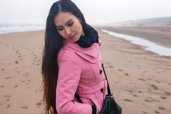 Portrait of attractive young woman with long beautiful hairs dressed pink coat, which posing in autumn North sea beach. — Stock Photo, Image