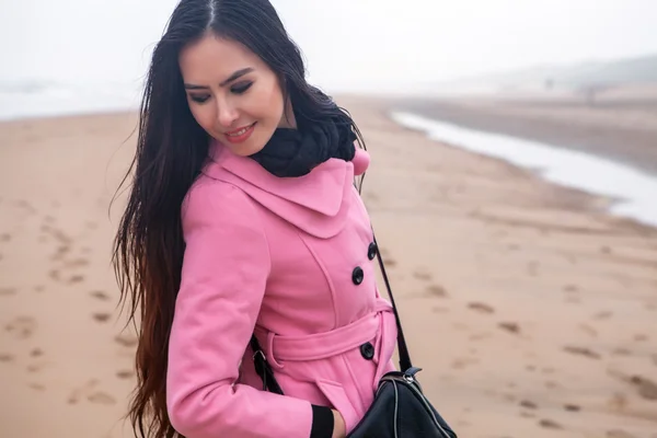 Portrait of attractive young woman with long beautiful hairs dressed pink coat, which posing in autumn North sea beach. — Stock Photo, Image