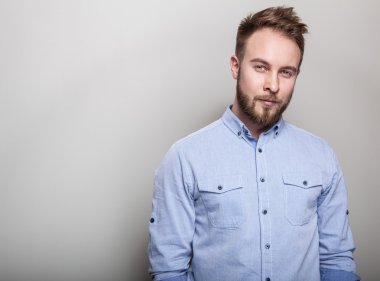 Mavi gömlekli genç yakışıklı samimi adam portresi. Açık gri renkli stüdyo fotoğrafı.