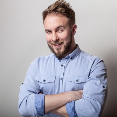 Mavi gömlekli genç yakışıklı samimi adam portresi. Açık gri renkli stüdyo fotoğrafı.