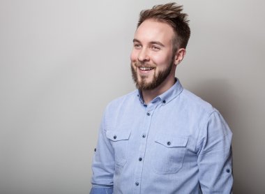 Mavi gömlekli genç yakışıklı samimi adam portresi. Açık gri renkli stüdyo fotoğrafı.