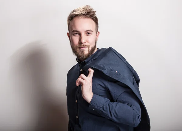 Elegante jonge knappe man in donker blauwe klassieke shirt en jas op zijn schouder. Studio fashion portret. — Stockfoto