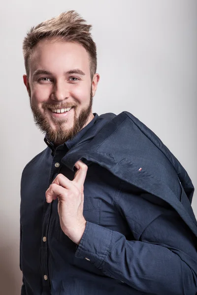 Κομψό όμορφος νεαρός άνδρας σε σκούρο μπλε κλασικό πουκάμισο και το σακάκι στον ώμο του. Στούντιο μόδας πορτρέτο. — Φωτογραφία Αρχείου