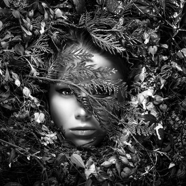 Fairy tale girl portrait surrounded with natural plants and flowers.Black-white art image in fantasy stylization.