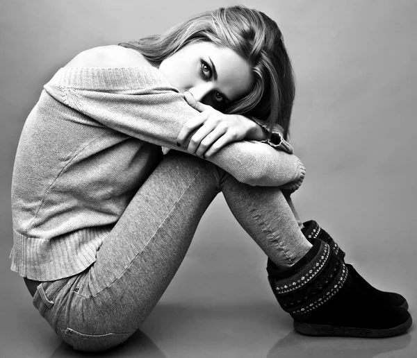 Mujer atractiva joven en ropa casual sentado en el piso del estudio. Foto en blanco y negro . —  Fotos de Stock