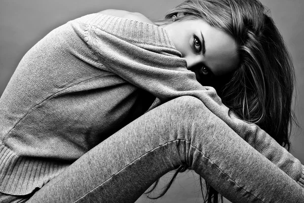Nuori viehättävä nainen rento vaatteita istuu studion lattialla. Musta-valkoinen kuva . — kuvapankkivalokuva
