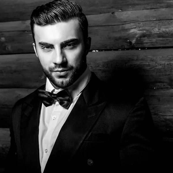 Retrato de joven hermoso hombre de moda contra la pared de madera En traje negro y corbata de lazo. Foto de moda blanco y negro sobre fondo de madera . — Foto de Stock