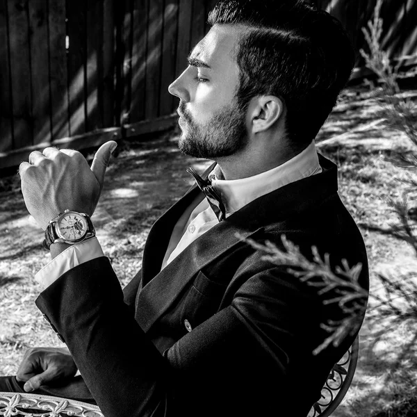 Retrato al aire libre del joven hombre europeo de moda posando cerca de la mesa de metal del jardín. Foto de moda blanco y negro . —  Fotos de Stock