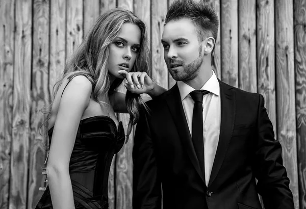 Porträt eines jungen attraktiven Paares, das im Freien vor hölzernem Hintergrund in schwarzer modischer Kleidung posiert. Schwarz-Weiß-Modefoto. Stockbild