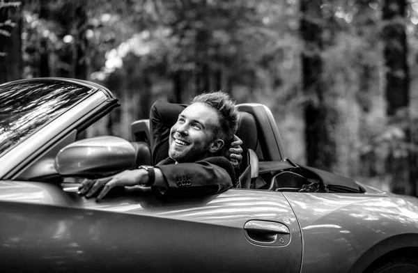 Elegante junge modische Mann in Cabrio-Auto im Freien. Schwarz-Weiß-Porträt. — Stockfoto