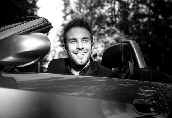 Elegant young fashionable man in convertible car outdoor. Black-white portrait. — Stock Photo, Image