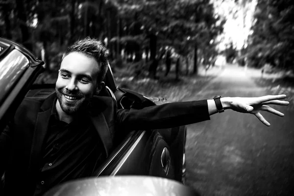 Elegante jovem elegante homem no carro conversível ao ar livre. Retrato preto-branco . — Fotografia de Stock