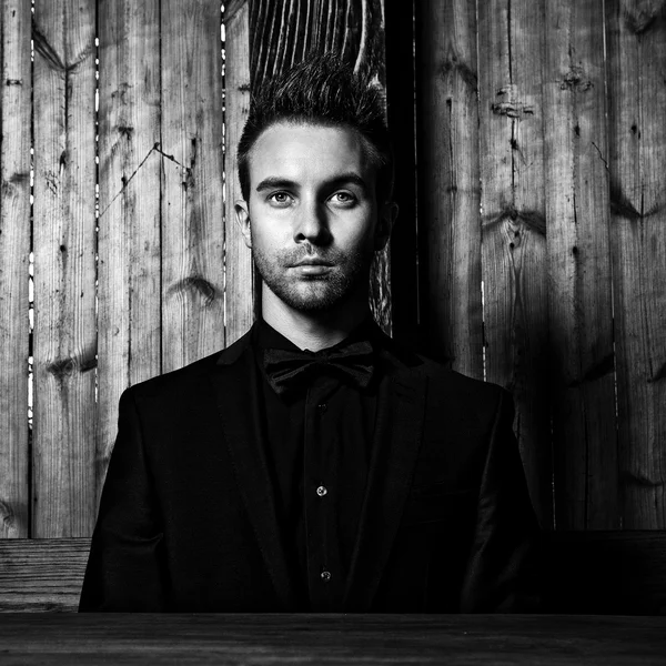 Retrato de joven hermoso hombre de moda contra la pared de madera En traje negro y corbata de lazo. Foto de moda blanco y negro sobre fondo de madera . —  Fotos de Stock