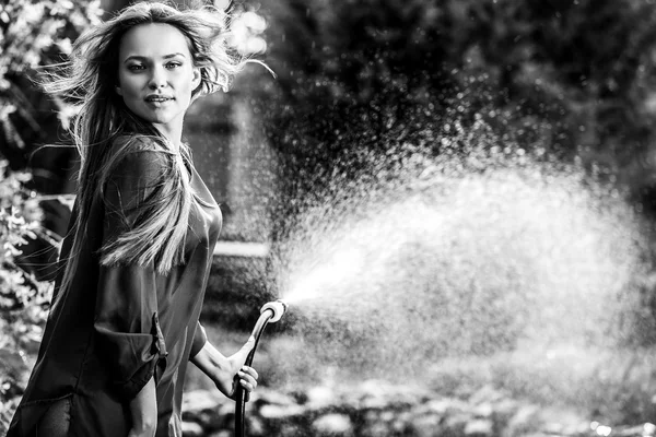 Mooie vrolijke jonge meid vormt in de zomertuin met een waterslang. Zwart-wit foto. — Stockfoto