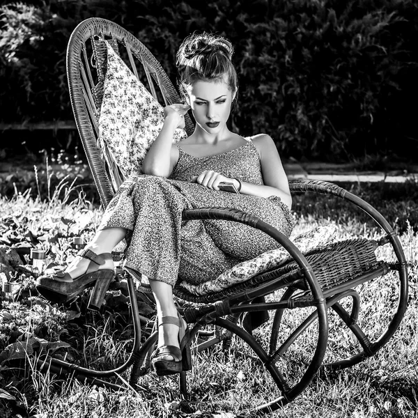 All'aperto ritratto di bella giovane donna che siede in rattan sedia a dondolo nel giardino estivo sera. Foto in bianco e nero . — Foto Stock