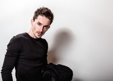 Siyah t-shirt ve deri ceket ışık gri stüdyo arka plan üzerinde poz onun elinde çekici şık adam.