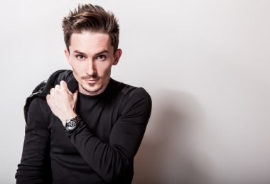 Siyah t-shirt ve deri ceket ışık gri stüdyo arka plan üzerinde poz onun elinde çekici şık adam.