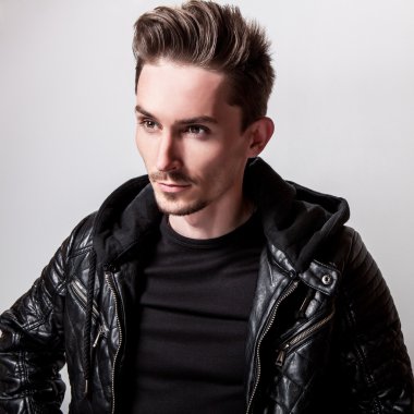 Işık gri arka plan üzerinde poz şık siyah deri ceketli çekici şık adamı.