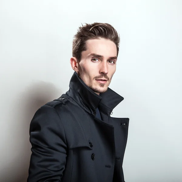 Elegantní mladý pohledný muž v dlouhé elegantní tmavě modrém kabátě. Portrét módní Studio. — Stock fotografie
