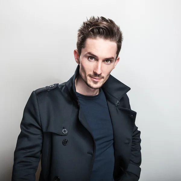 Elegante homem bonito jovem em casaco azul escuro elegante longo. Estúdio retrato de moda . — Fotografia de Stock