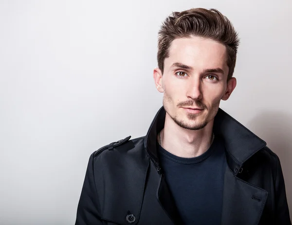 Eleganter junger gutaussehender Mann in langem, stylischem dunkelblauen Mantel. Modeporträt im Studio. — Stockfoto