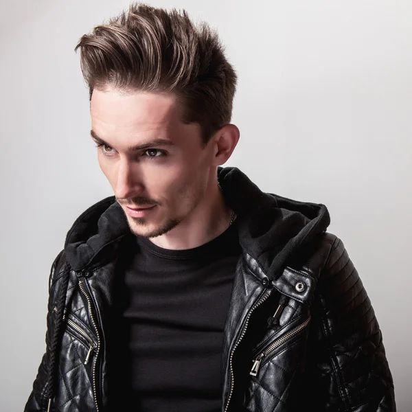 Işık gri arka plan üzerinde poz şık siyah deri ceketli çekici şık adamı.