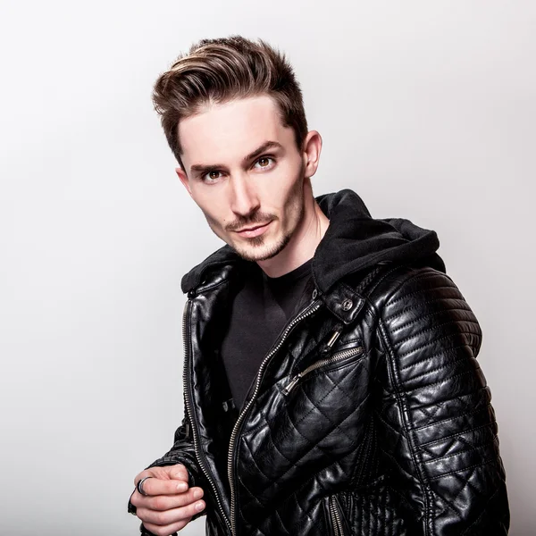 Atractivo hombre elegante en elegante chaqueta de cuero negro posando sobre fondo gris claro . — Foto de Stock